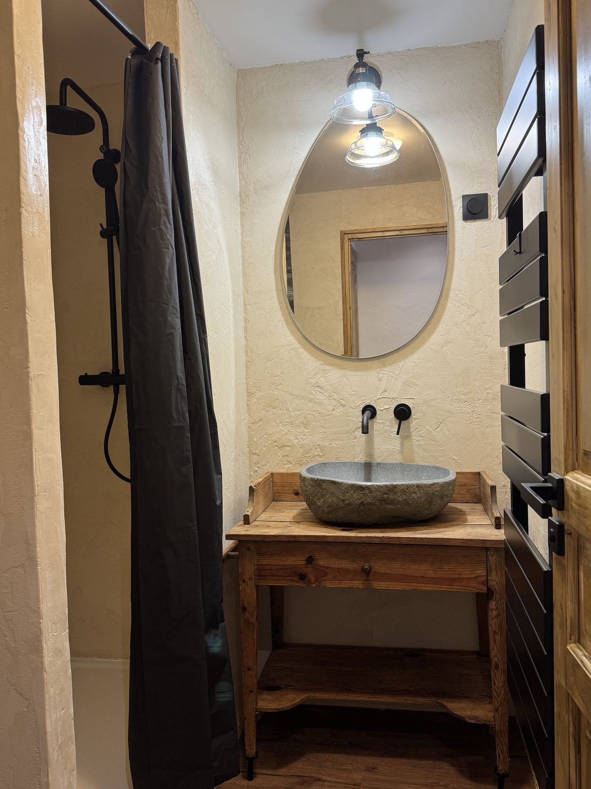 Salle de bain de l'appartement, vasque en pierre sur un meuble en vieux bois, miroir ovale et douche