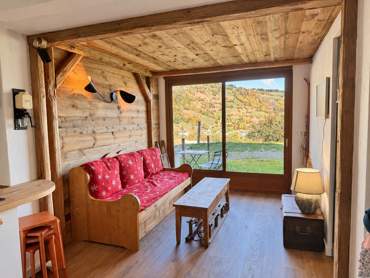 Salon de l'appartement, banquette en bois aux coussins rouges et baie vitrée sur la vallée