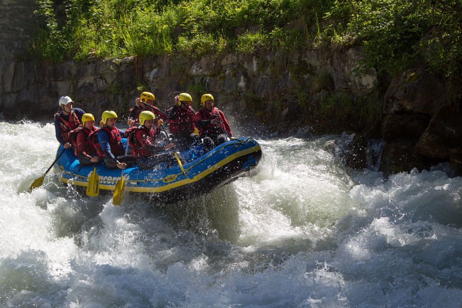 Équipe en raft bleu sur les rapides de l'Isère, casques jaunes et combinaisons rouges
