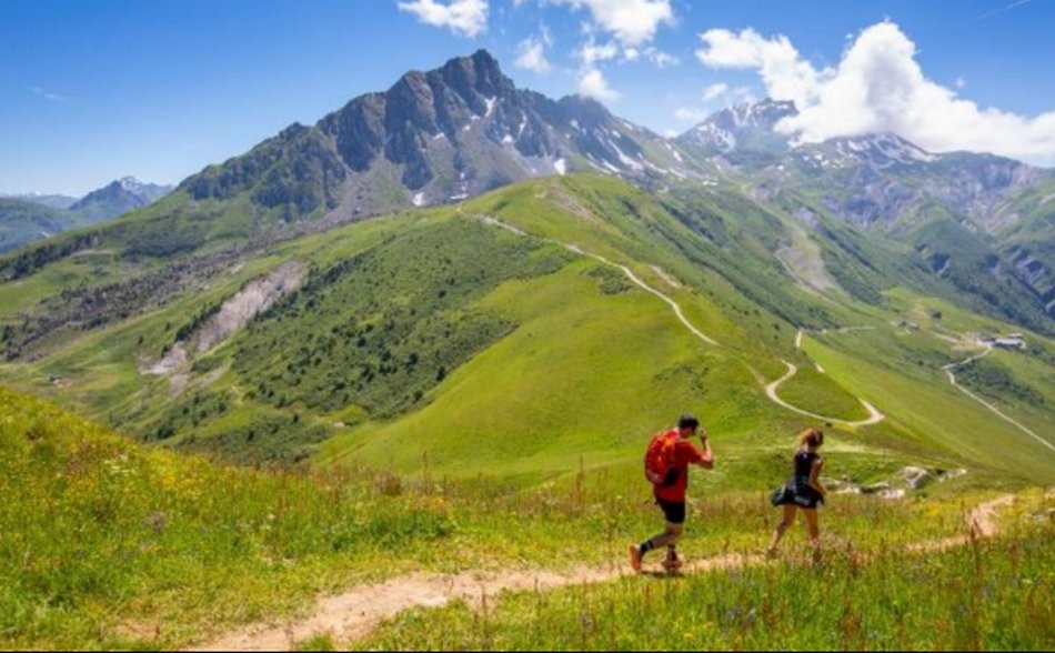 Randonneurs sur sentier alpin avec sac à dos rouge, alpage fleuri et Cheval Noir en arrière-plan